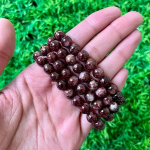 Könnte beinhalten: Ein Armband aus roten und weißen Edelsteinperlen. Die Perlen sind rund und haben eine gesprenkelte Optik.