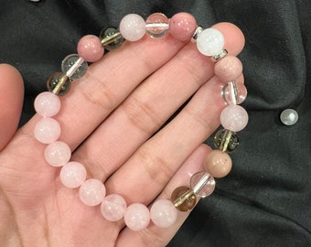 May include: A bracelet made of pink, clear, and brown gemstone beads. The bracelet has a silver charm.