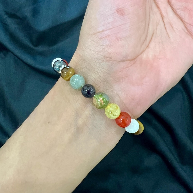 May include: A bracelet with a variety of colorful gemstone beads, including green, red, yellow, and brown. The bracelet is made with a silver clasp.