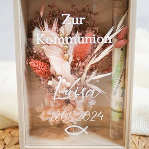 K&ouml;nnte beinhalten: Eine Holzkiste mit einer Glasfront, die getrocknete Blumen, ein kleines Glasr&ouml;hrchen mit Geld darin und den Text "Zur Kommunion Lisa 18.05.2024" auf dem Glas enth&auml;lt.