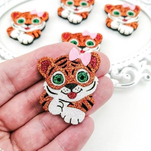 May include: Five orange and brown glitter tiger face appliques with pink bows. The tiger faces have green eyes and white glitter accents.
