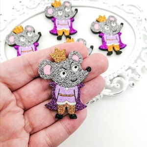 Op de afbeelding: Vijf glitterende muisfiguren met gouden kronen en paarse mantels. De muizen dragen gouden broeken en hebben roze oren.