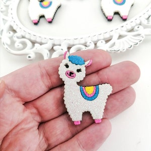 May include: A white glitter llama with pink hooves, blue ears, and a yellow, pink, and blue striped saddle. The llama is a craft supply and is made of wood.