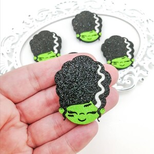 Może przedstawiać: Cztery wycięte postacie Frankensteina z czarnego i zielonego brokatu z białymi akcentami. Postacie mają zielone twarze z czarnymi oczami i białymi rzęsami. Postacie mają czarne włosy z białymi akcentami.