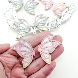 May include: A set of eight wooden butterfly shapes with a glitter finish. The butterflies are in various pastel colors, including pink, blue, and green.