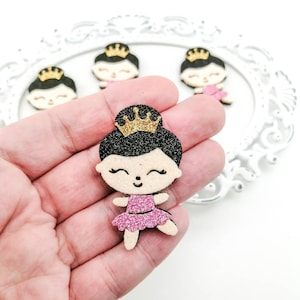 Könnte beinhalten: Eine rosa Glitzer-Ballerina mit einer goldenen Glitzerkrone und schwarzen Glitzerhaaren. Die Ballerina hält ihre Arme ausgestreckt und hat einen fröhlichen Gesichtsausdruck.