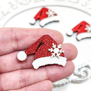 Peut inclure: Chapeau de Père Noël rouge pailleté avec un pompon blanc et un flocon de neige blanc sur le dessus. Le chapeau est en feutre et mesure environ 5 cm de haut.