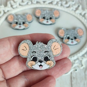 Puede incluir: Cinco adornos de cabeza de ratón de purpurina plateada con mejillas rosadas y orejas melocotón. Las cabezas de ratón están sobre un fondo blanco.