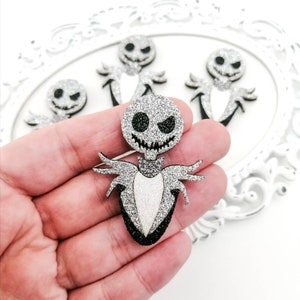Peut inclure: Personnage de Jack Skellington en paillettes argentées avec des détails noirs. Le personnage tient une cravate rayée noire et blanche.
