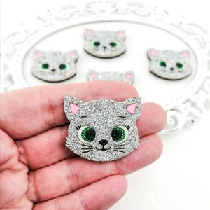 May include: Silver glitter cat face with pink ears and green eyes. The cat face is on a white background.