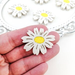 Op de afbeelding: Een witte glitter madeliefje met een gele kern. De madeliefje is ongeveer 5 cm in diameter.
