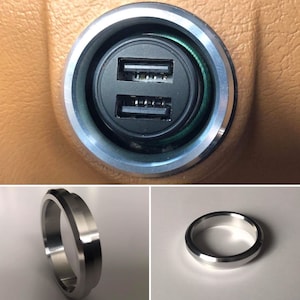 May include: Close-up of a silver-colored car charger with two USB ports. The charger is mounted in a circular opening in a brown leather surface.