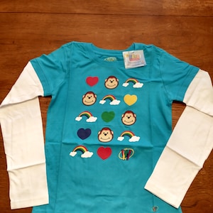 May include: A turquoise long-sleeved shirt with white sleeves. The shirt has a colorful design with monkeys, hearts, and rainbows. The shirt has the text "Livz" on the tag.