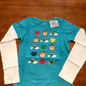May include: A turquoise long-sleeved shirt with white sleeves. The shirt has a colorful design with monkeys, hearts, and rainbows. The shirt has the text "Livz" on the tag.