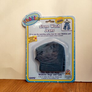 May include: A blue stone wash jeans outfit for a Webkinz pet. The outfit is packaged on a card with the Webkinz logo and the words "Stone Wash Jeans".