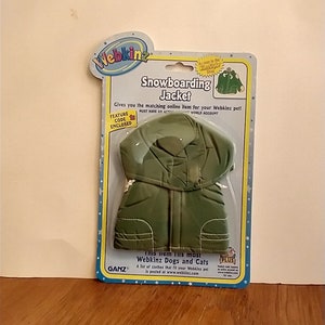 Puede incluir: Chaqueta de snowboard Webkinz verde para perros y gatos. El paquete presenta una imagen de la chaqueta y el texto "Este artículo se adapta a la mayoría de los perros y gatos Webkinz".