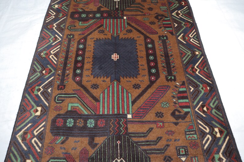 May include: A brown rug with a geometric pattern in shades of red, green, blue, and black. The rug has a central diamond shape with a smaller diamond inside. The rug has a border with a repeating pattern.