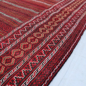 Puede incluir: Primer plano de una alfombra tejida roja, negra y blanca con intrincados patrones geom&eacute;tricos. La alfombra tiene un borde con flecos y est&aacute; doblada por la mitad.
