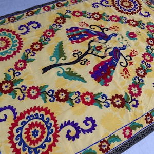 May include: A yellow fabric wall hanging with a colorful embroidered design featuring two peacocks on a tree branch. The design also includes floral motifs and geometric patterns.