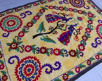 May include: A yellow fabric wall hanging with a colorful embroidered design featuring two peacocks on a tree branch. The design also includes floral motifs and geometric patterns.