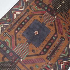 May include: A brown rug with a geometric pattern in shades of red, green, blue, and white. The rug has a central diamond shape with a smaller diamond in the centre.