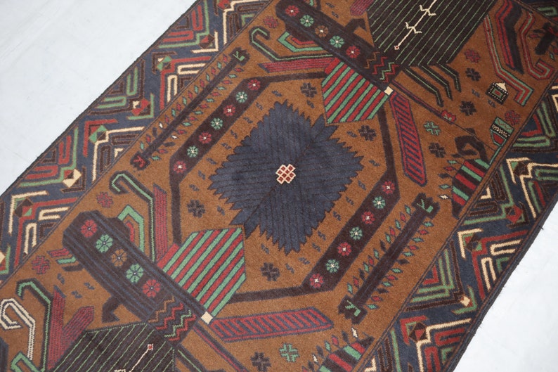 May include: A brown rug with a geometric pattern in shades of red, green, blue, and white. The rug has a central diamond shape with a smaller diamond in the centre.