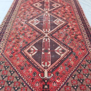 Puede incluir: Una alfombra larga y rectangular con un patr&oacute;n de diamante central en tonos de rojo, marr&oacute;n y crema. La alfombra presenta intrincados dise&ntilde;os geom&eacute;tricos y un borde con motivos florales. La paleta de colores de la alfombra incluye rojos intensos, marrones y toques de crema.