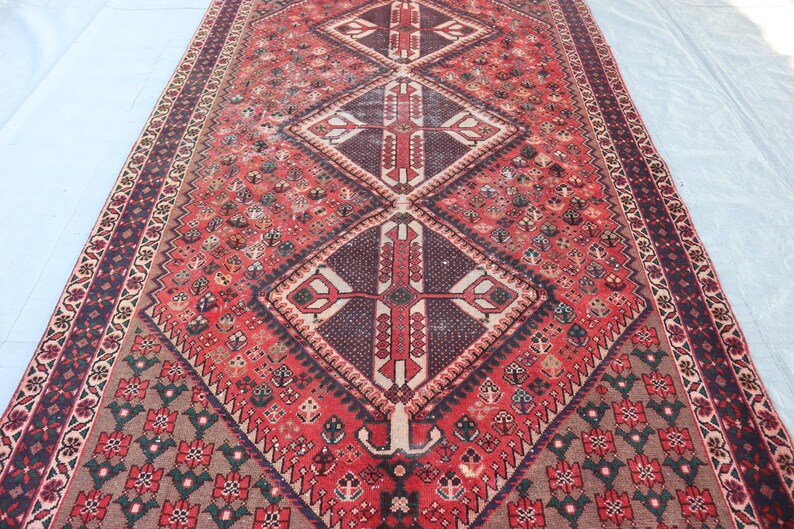 Puede incluir: Una alfombra larga y rectangular con un patr&oacute;n de diamante central en tonos de rojo, marr&oacute;n y crema. La alfombra presenta intrincados dise&ntilde;os geom&eacute;tricos y un borde con motivos florales. La paleta de colores de la alfombra incluye rojos intensos, marrones y toques de crema.