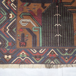 May include: A brown, blue, green and cream patterned rug with a fringed border. The rug features geometric designs and a central motif of a stylised tree.