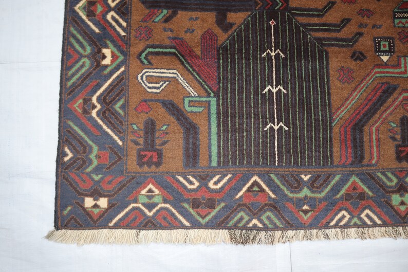 May include: A brown, blue, green and cream patterned rug with a fringed border. The rug features geometric designs and a central motif of a stylised tree.