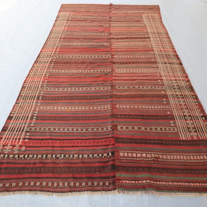 May include: A long, rectangular rug with a striped pattern in shades of red, brown, and white. The rug has a fringe border.