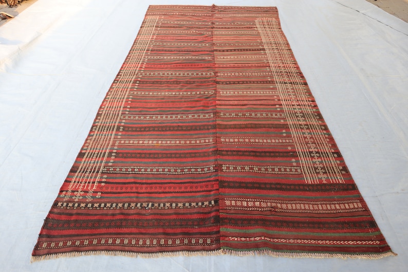 May include: A long, rectangular rug with a striped pattern in shades of red, brown, and white. The rug has a fringe border.