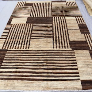 May include: A rectangular area rug featuring a geometric pattern of alternating dark brown and cream-colored blocks. The design consists of sections with horizontal or vertical stripes of varying widths, creating a textured, high-contrast visual effect.