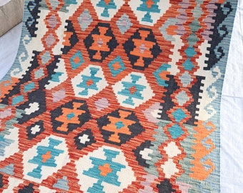 May include: A colorful rug with a geometric pattern in shades of red, orange, blue, black, and white. The rug has a fringed edge.