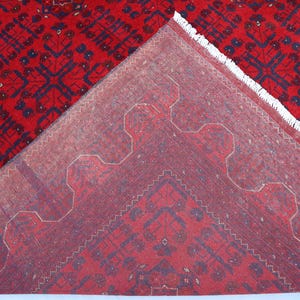 Op de afbeelding: Close-up van de achterkant van een rood tapijt met een blauw en wit geometrisch patroon. Het tapijt heeft een franje rand.