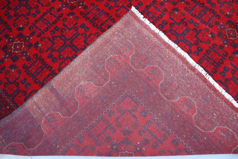 Op de afbeelding: Close-up van de achterkant van een rood tapijt met een blauw en wit geometrisch patroon. Het tapijt heeft een franje rand.