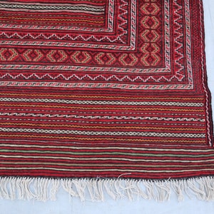 Puede incluir: Una alfombra roja, negra y blanca con flecos. La alfombra tiene un dise&ntilde;o geom&eacute;trico y est&aacute; hecha de lana.