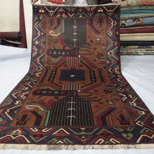 May include: A brown, black, green and red patterned rug with a geometric design. The rug has a fringed border.