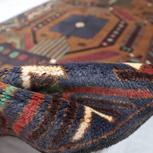 May include: Close-up of a folded blue, brown, red and white patterned rug with a fringed edge. The rug has a geometric design.