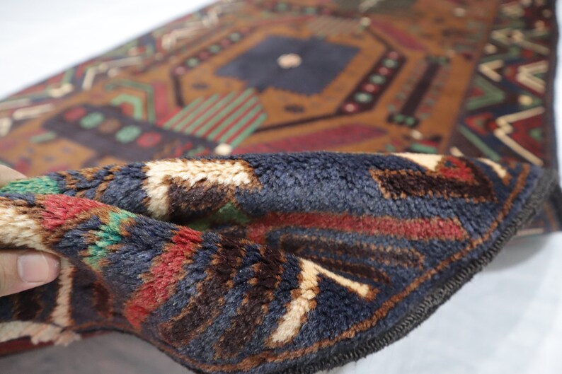 May include: Close-up of a folded blue, brown, red and white patterned rug with a fringed edge. The rug has a geometric design.