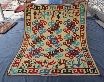 May include: A colorful hand-woven rug with a geometric pattern featuring stylized animals and floral motifs. The rug has a cream background with red, blue, and yellow accents.
