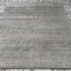 Puede incluir: Una alfombra rectangular en un tono gris sólido y apagado. La superficie presenta una textura sutil y uniforme con ligeras variaciones de sombreado en todo el pelo, creando una apariencia suave y monocromática en toda la pieza rectangular.