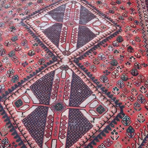 Puede incluir: Una alfombra antigua detallada con una combinaci&oacute;n de colores rojo y burdeos. La alfombra presenta un patr&oacute;n de diamante central con un dise&ntilde;o en forma de cruz, rodeado de intrincados motivos florales y geom&eacute;tricos. Los bordes tienen un borde detallado.