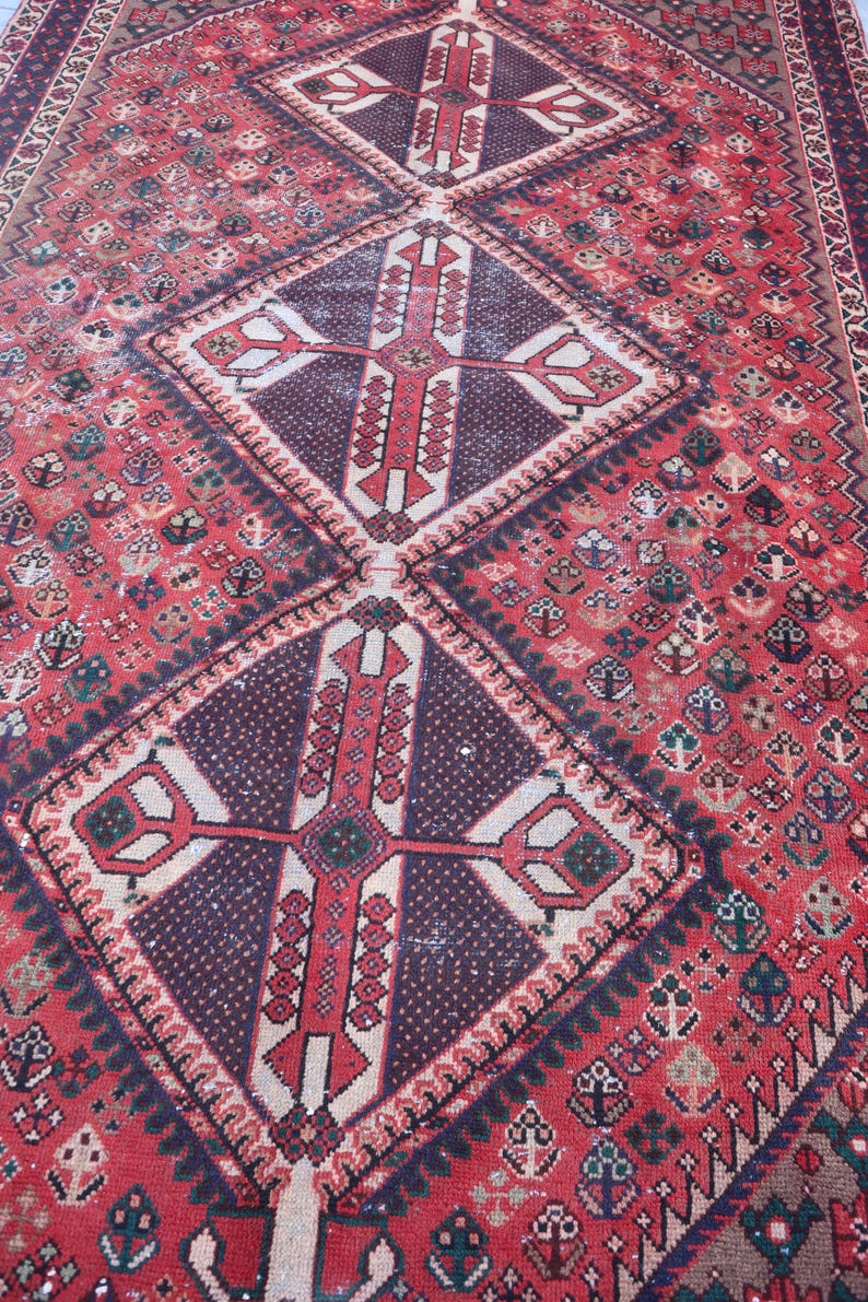 Puede incluir: Una alfombra antigua detallada con una combinaci&oacute;n de colores rojo y burdeos. La alfombra presenta un patr&oacute;n de diamante central con un dise&ntilde;o en forma de cruz, rodeado de intrincados motivos florales y geom&eacute;tricos. Los bordes tienen un borde detallado.