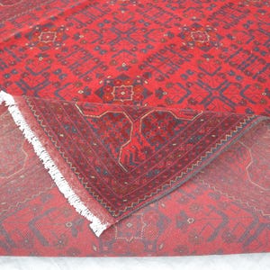 Op de afbeelding: Een rood tapijt met een traditioneel Perzisch ontwerp. Het tapijt heeft een witte franje en is doormidden gevouwen, waardoor de achterkant van het tapijt zichtbaar is.