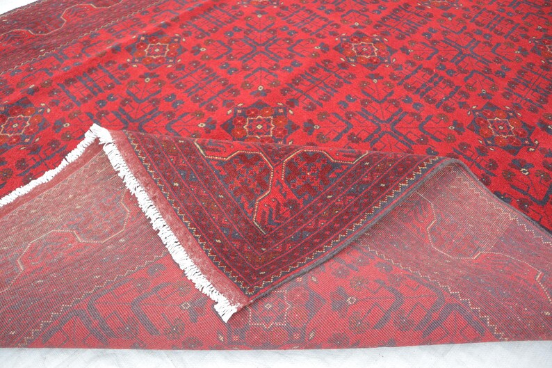 Op de afbeelding: Een rood tapijt met een traditioneel Perzisch ontwerp. Het tapijt heeft een witte franje en is doormidden gevouwen, waardoor de achterkant van het tapijt zichtbaar is.