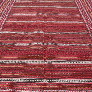 Puede incluir: Una alfombra roja, blanca y negra a rayas con intrincados patrones geom&eacute;tricos en el borde. La alfombra tiene un aspecto y una sensaci&oacute;n tradicionales tejidos.