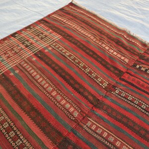 May include: A red, green, and black striped rug with intricate geometric patterns woven into the fabric. The rug has a frayed edge and appears to be handmade.