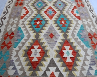 May include: A white rug with a geometric pattern in shades of red, orange, blue, and purple. The pattern is made up of diamonds, triangles, and squares.