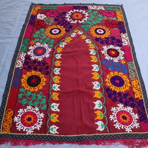 May include: A traditional Turkish prayer rug with a burgundy background and intricate embroidery in shades of red, yellow, green, blue, and white. The rug features a central archway design with floral motifs and geometric patterns.